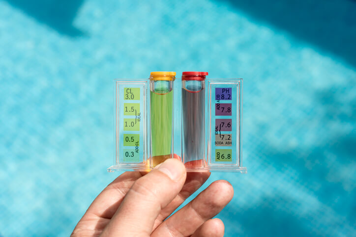 Hand holding pool water test in front of blue pool water in background